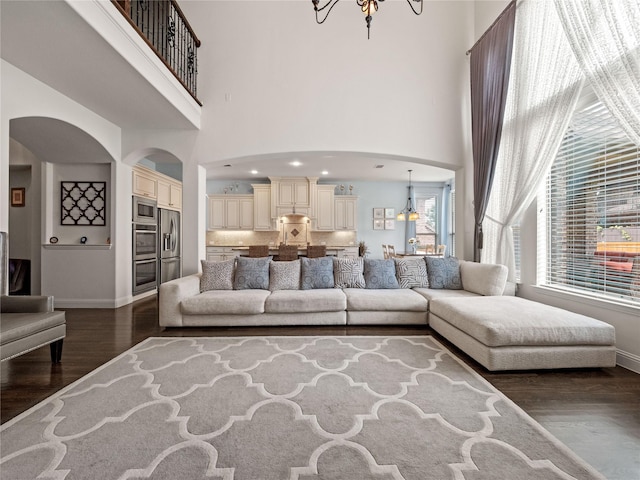 1504 Cayman Dr, Allen, TX 75013 - living room featuring arched walkways, dark wood-style floors, a towering ceiling, baseboards, and a chandelier