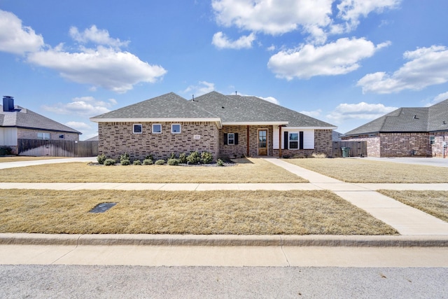 view of front of property featuring brick siding, a shingled roof, a front lawn, and fence