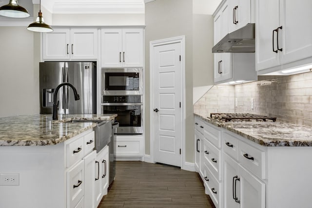 kitchen featuring light stone countertops, ornamental molding, under cabinet range hood, appliances with stainless steel finishes, and tasteful backsplash