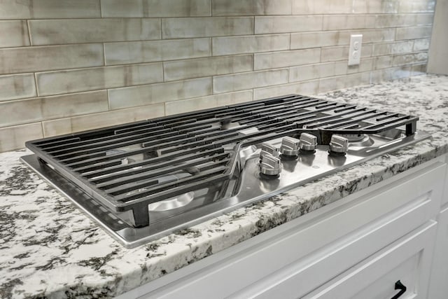 interior details featuring light stone counters, backsplash, and stainless steel gas stovetop