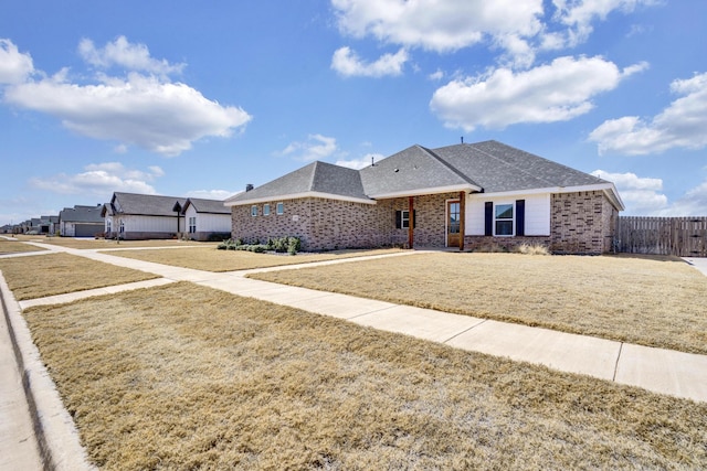 view of front of property with brick siding, roof with shingles, a front lawn, and fence