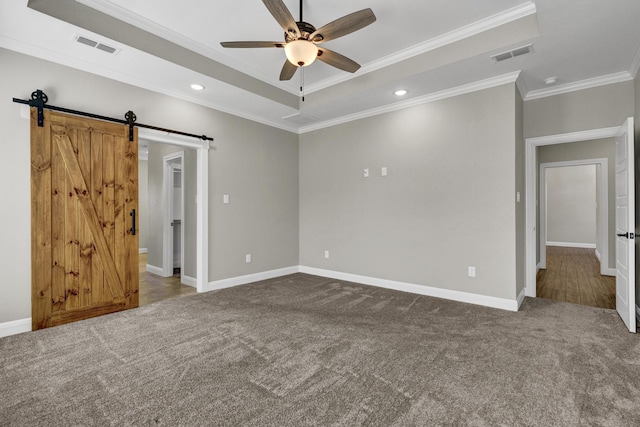 carpeted empty room featuring a tray ceiling, visible vents, a barn door, and crown molding