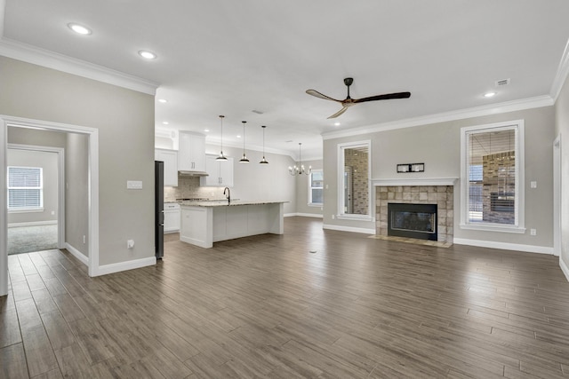 unfurnished living room featuring a sink, dark wood-type flooring, ceiling fan with notable chandelier, and ornamental molding