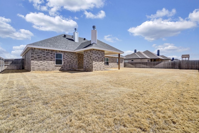 rear view of property featuring a yard, a chimney, a fenced backyard, and brick siding