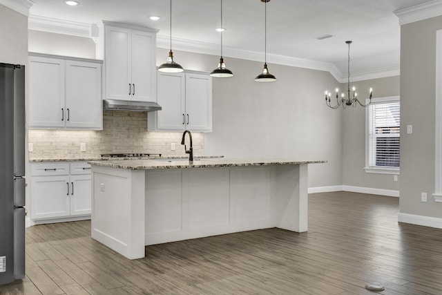 kitchen featuring under cabinet range hood, ornamental molding, decorative backsplash, freestanding refrigerator, and wood finished floors