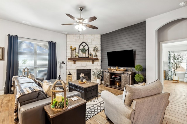 living room with visible vents, light wood-style flooring, a ceiling fan, a stone fireplace, and baseboards