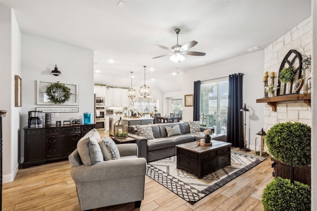 living area featuring a stone fireplace, ceiling fan with notable chandelier, light wood-style floors, and visible vents