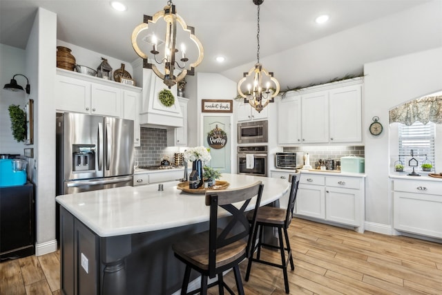 kitchen featuring white cabinetry, appliances with stainless steel finishes, light wood finished floors, light countertops, and vaulted ceiling