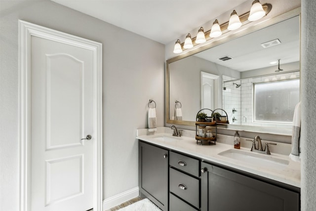 bathroom with double vanity, visible vents, a tile shower, and a sink