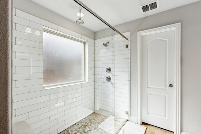 full bath with a tile shower, visible vents, and wood finished floors