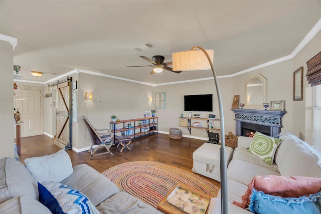 living area featuring a ceiling fan, wood finished floors, visible vents, ornamental molding, and a barn door