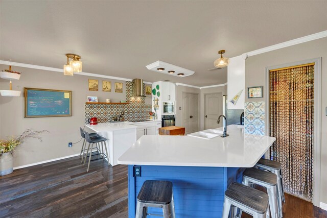 kitchen featuring black appliances, ornamental molding, a sink, a breakfast bar area, and wall chimney range hood