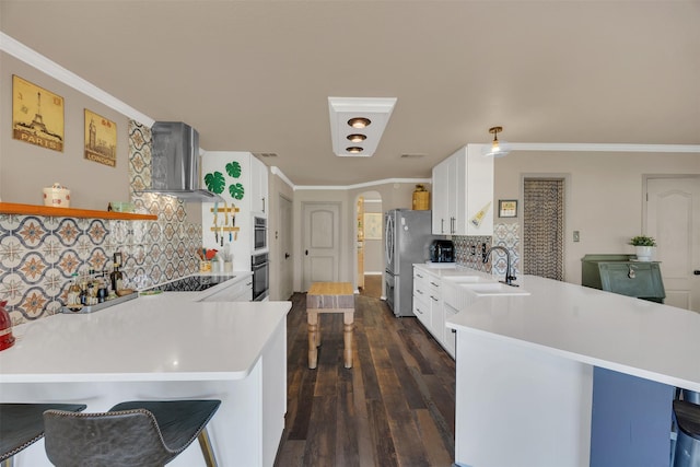 kitchen with arched walkways, a peninsula, wall chimney exhaust hood, and ornamental molding