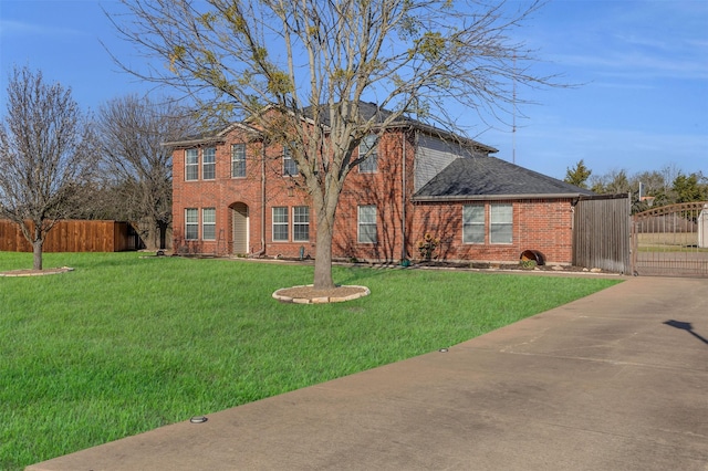 colonial home featuring brick siding, a gate, a front yard, and fence