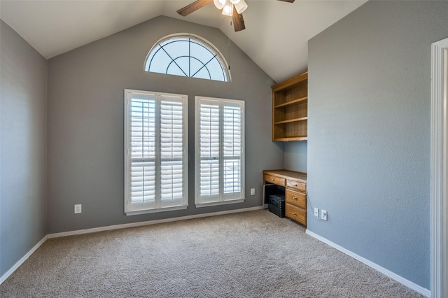 unfurnished office with light carpet, lofted ceiling, built in desk, baseboards, and ceiling fan