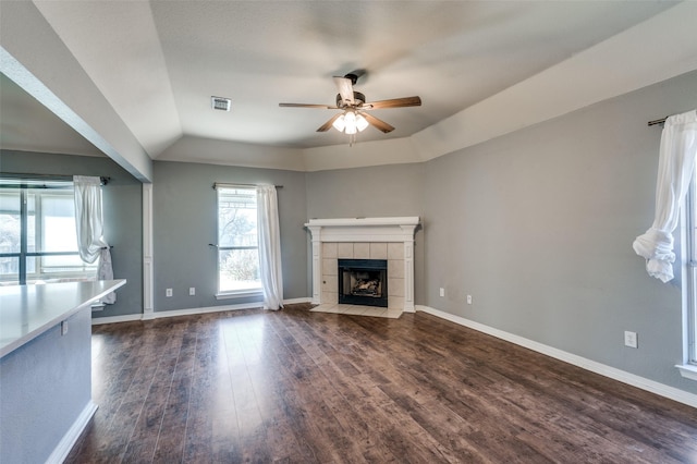 unfurnished living room with visible vents, baseboards, a tiled fireplace, a ceiling fan, and dark wood-style flooring