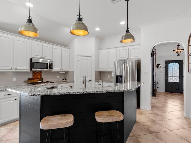 kitchen featuring arched walkways, stainless steel appliances, an island with sink, and tasteful backsplash