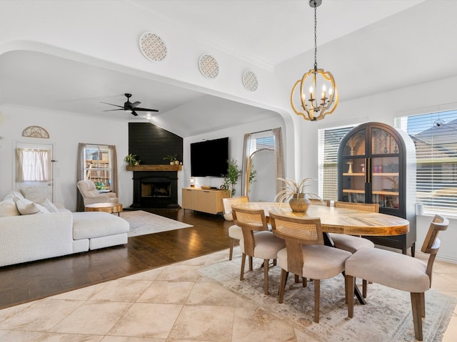 dining area with lofted ceiling, arched walkways, tile patterned floors, ceiling fan with notable chandelier, and a large fireplace