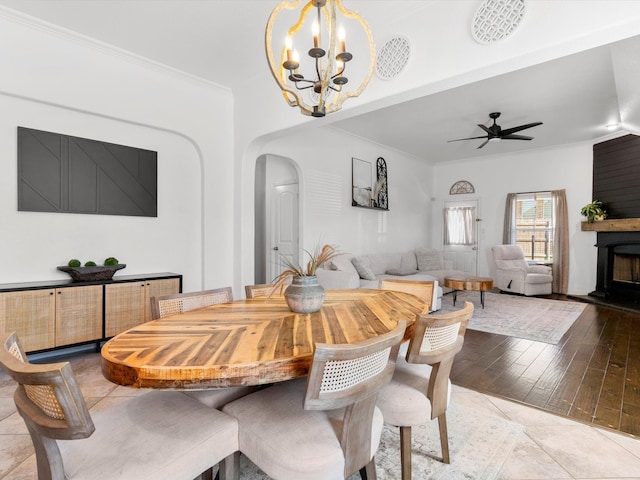 dining area with a large fireplace, arched walkways, crown molding, and ceiling fan with notable chandelier