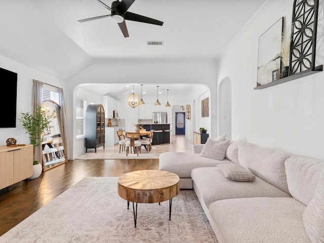 living room featuring visible vents, light wood-type flooring, lofted ceiling, ceiling fan with notable chandelier, and arched walkways