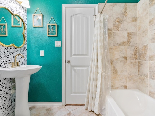 full bath featuring a sink, shower / bath combination with curtain, baseboards, tile patterned flooring, and a textured wall