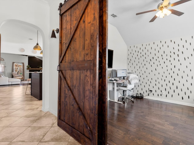 office featuring visible vents, a barn door, baseboards, ceiling fan, and vaulted ceiling