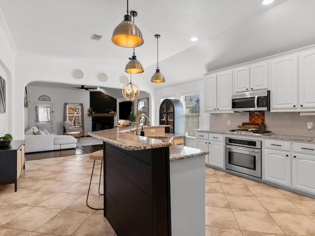 kitchen with backsplash, open floor plan, arched walkways, appliances with stainless steel finishes, and a fireplace