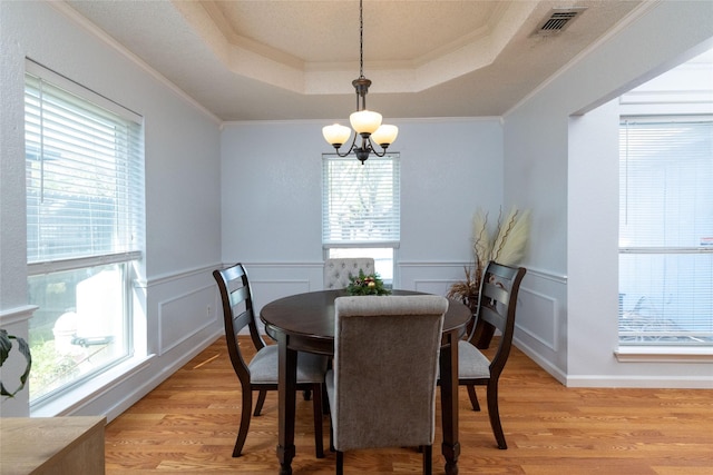 dining space with a wealth of natural light, a raised ceiling, light wood-style floors, and a chandelier