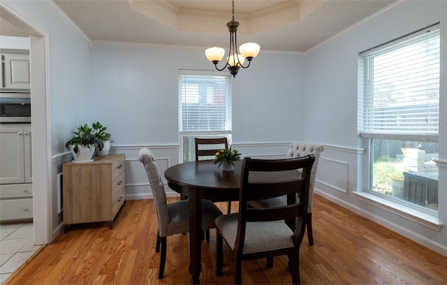 dining area featuring a wealth of natural light, a tray ceiling, crown molding, and light wood finished floors