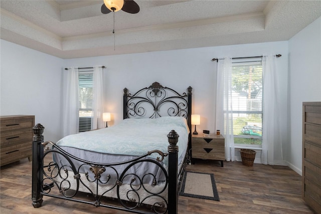 bedroom featuring a tray ceiling, a textured ceiling, wood finished floors, crown molding, and baseboards