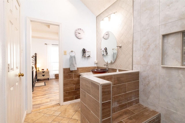 ensuite bathroom with tile patterned floors, a sink, ensuite bath, tile walls, and lofted ceiling