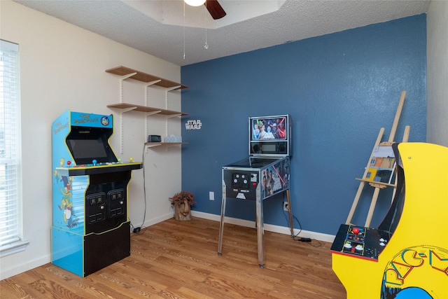 recreation room featuring a ceiling fan, wood finished floors, baseboards, and a textured ceiling