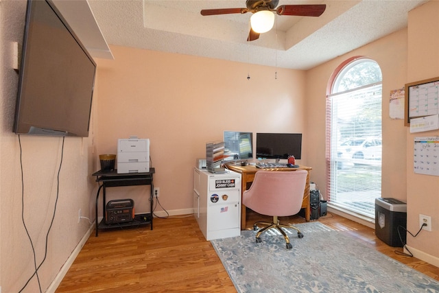 home office featuring a tray ceiling, baseboards, light wood-type flooring, and a textured ceiling