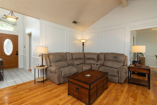 living area featuring visible vents, light wood-type flooring, lofted ceiling, a decorative wall, and a textured ceiling