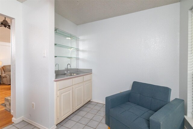 bar with a sink, a textured ceiling, wet bar, light tile patterned floors, and baseboards