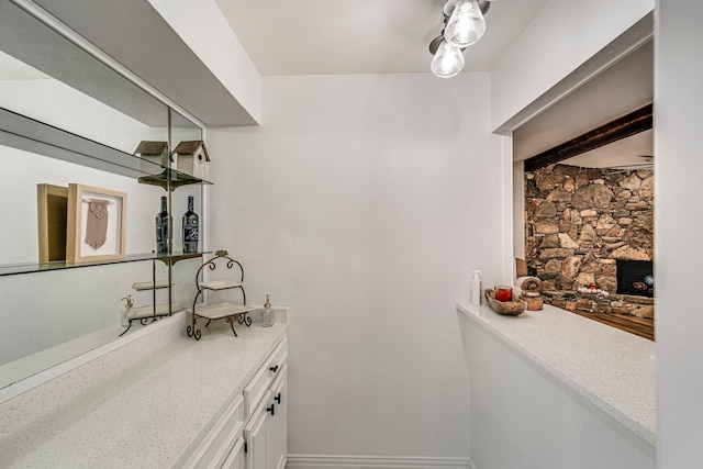 bathroom featuring beamed ceiling, baseboards, and a stone fireplace