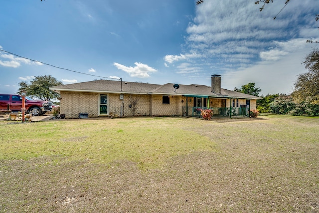 rear view of property featuring brick siding, a lawn, and a chimney