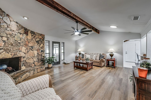 living room with baseboards, visible vents, light wood finished floors, vaulted ceiling with beams, and a stone fireplace