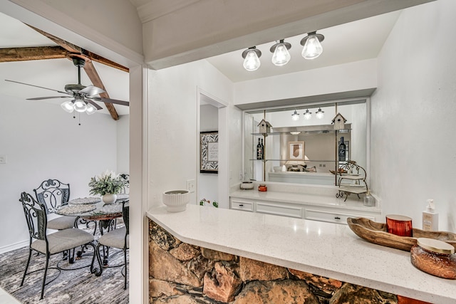 interior space featuring lofted ceiling with beams, white cabinets, light stone counters, and a ceiling fan