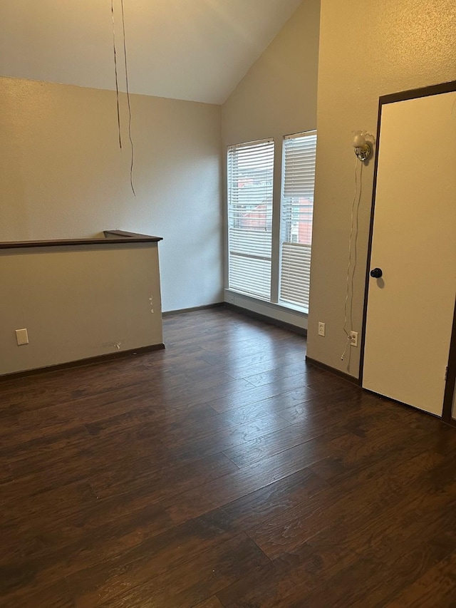 empty room featuring baseboards, lofted ceiling, and dark wood finished floors