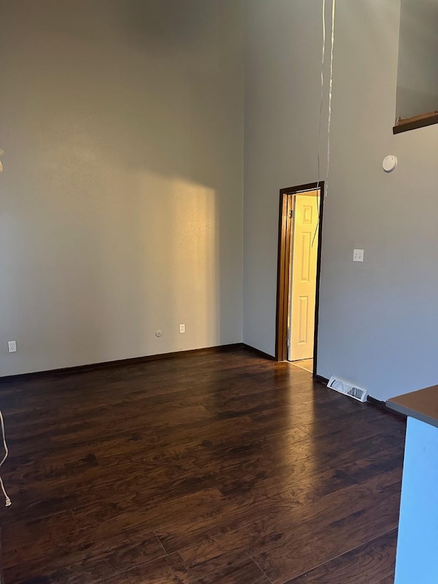 spare room featuring dark wood-style floors, visible vents, a high ceiling, and baseboards