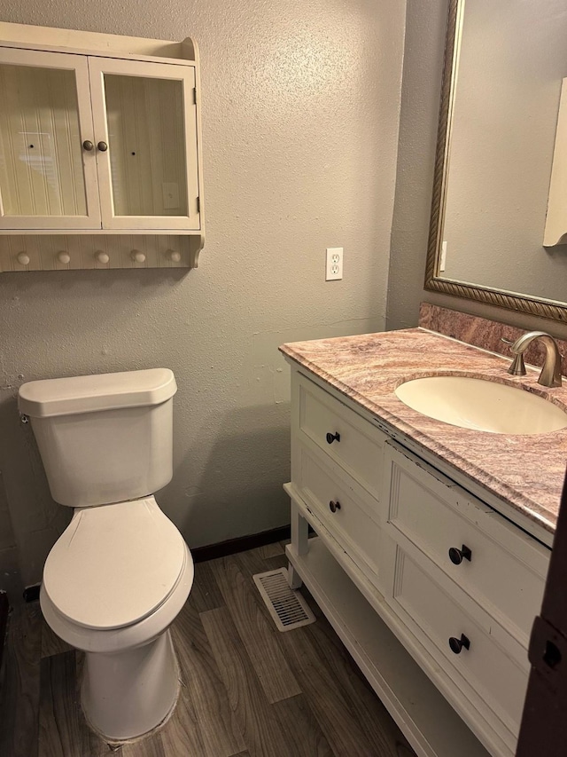 half bathroom featuring vanity, toilet, wood finished floors, and a textured wall