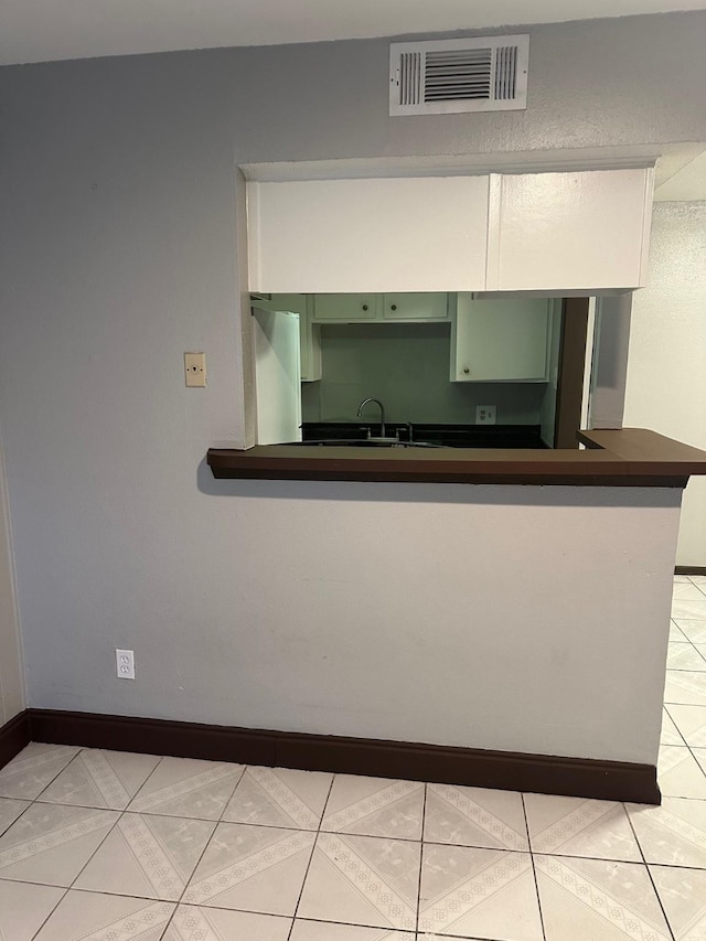 kitchen with dark countertops, visible vents, green cabinetry, light tile patterned flooring, and fridge