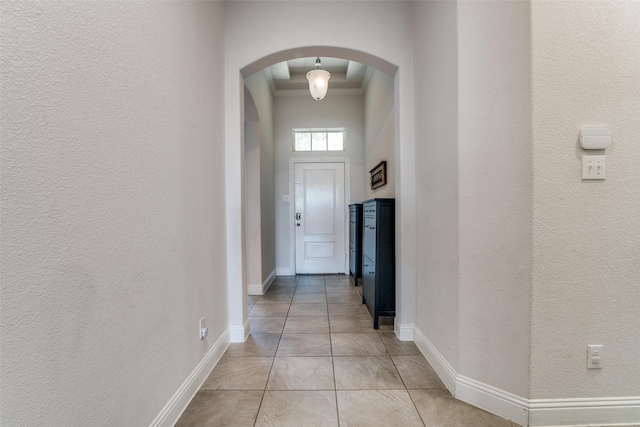 hall featuring baseboards, arched walkways, crown molding, and a textured wall