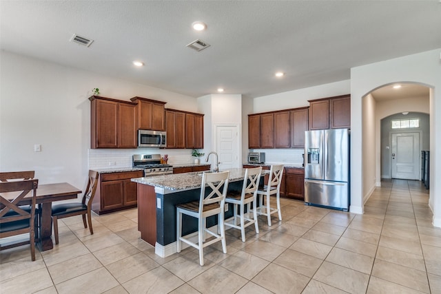 kitchen with visible vents, an island with sink, stainless steel appliances, arched walkways, and a breakfast bar area