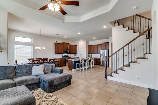 living room featuring stairway, light tile patterned floors, a tray ceiling, recessed lighting, and ceiling fan with notable chandelier