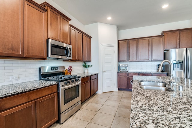 kitchen with light tile patterned floors, light stone countertops, a sink, decorative backsplash, and appliances with stainless steel finishes