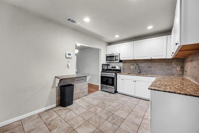 kitchen featuring a sink, tasteful backsplash, stainless steel appliances, dark stone counters, and white cabinets