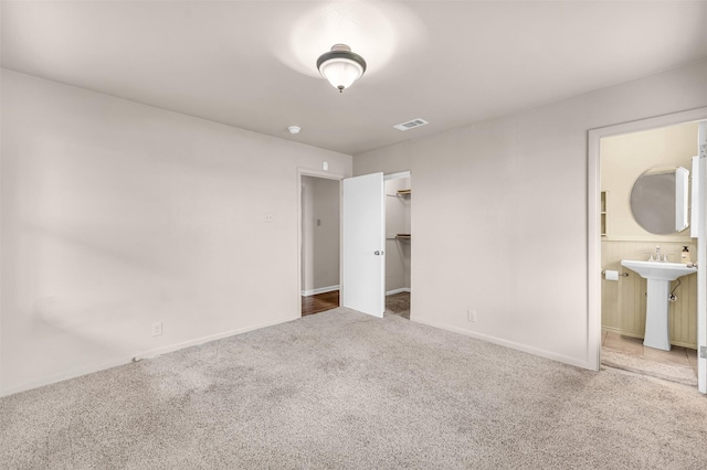 unfurnished bedroom featuring visible vents, baseboards, carpet flooring, ensuite bath, and a sink