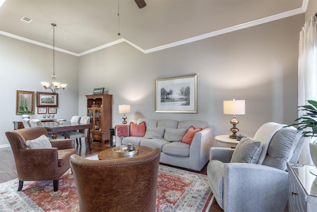 living room featuring wood finished floors, baseboards, visible vents, ornamental molding, and ceiling fan with notable chandelier